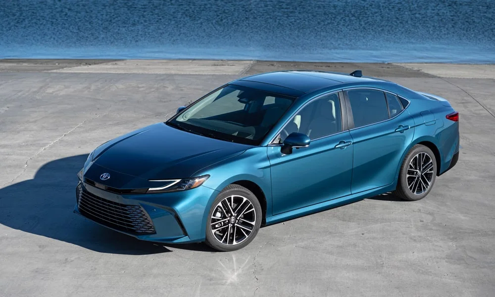Фото Toyota Camry (2024) — вид спереди, фото 10. Кузов в синем цвете: рисунок оптики и решётки задаёт узнаваемое «лицо» модели. Рисунок ходовых огней — подпись модели, по нему её узнают в потоке Toyota Camry (2024) — вид спереди, фото 10