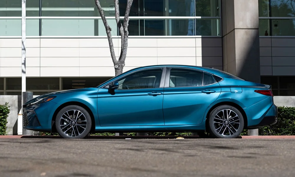 Фото Toyota Camry (2024) — вид сбоку, фото 2. Профиль в синем цвете: соотношение колёсной базы и свесов. Хромированные или чёрные молдинги окон отличают комплектации Toyota Camry (2024) — вид сбоку, фото 2