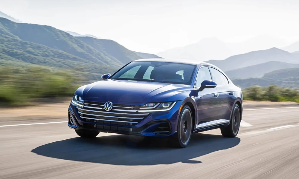 Фото Volkswagen Arteon (2024) — вид спереди, фото 4. Передок в синем исполнении — крупная светотехника и выразительный бампер. Рисунок ходовых огней — подпись модели, по нему её узнают в потоке Volkswagen Arteon (2024) — вид спереди, фото 4