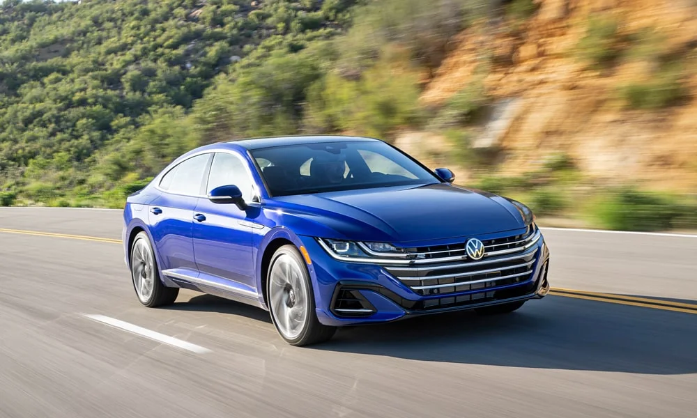 Фото Volkswagen Arteon (2024) — вид спереди, фото 5. Синий кузов, строгая симметрия оптики — базовый ракурс знакомства с дизайном. Дневные ходовые огни включаются автоматически с запуском Volkswagen Arteon (2024) — вид спереди, фото 5
