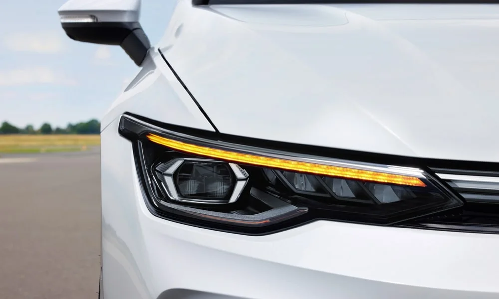 Фото Volkswagen Golf (2024) — вид спереди, фото 5. Кузов в белом цвете: рисунок оптики и решётки задаёт узнаваемое «лицо» модели. Рисунок ходовых огней — подпись модели, по нему её узнают в потоке Volkswagen Golf (2024) — вид спереди, фото 5