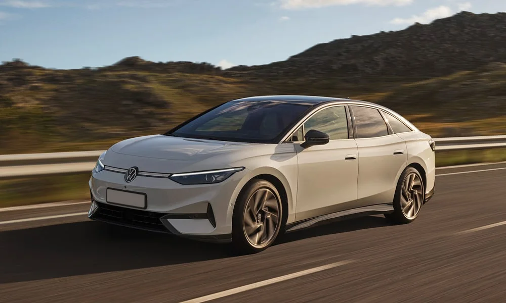 Фото Volkswagen ID 7 (2024) — вид спереди, фото 5. Кузов в белом цвете: рисунок оптики и решётки задаёт узнаваемое «лицо» модели. Дневные ходовые огни включаются автоматически с запуском Volkswagen ID 7 (2024) — вид спереди, фото 5