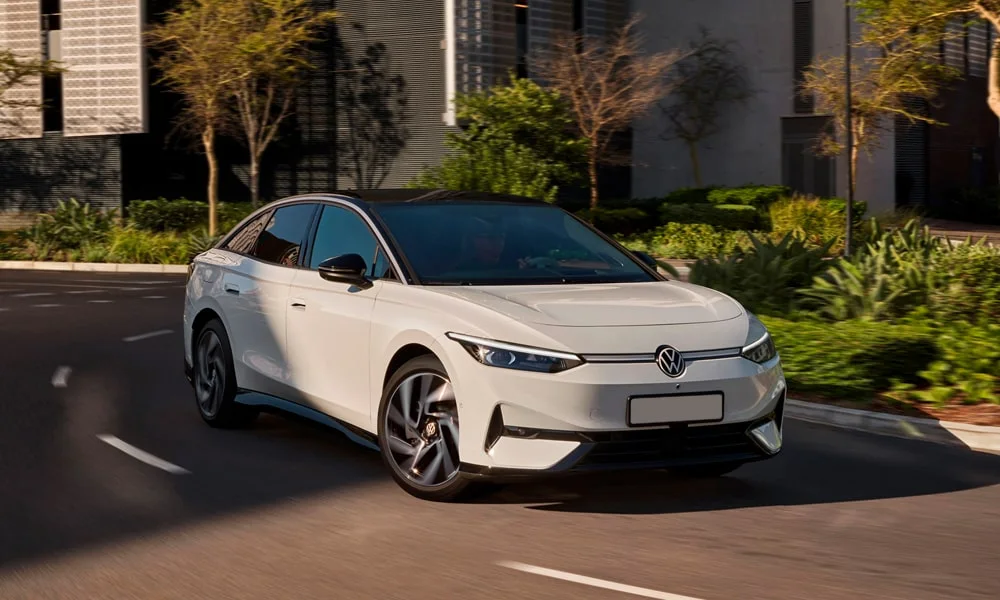 Фото Volkswagen ID 7 (2024) — вид спереди, фото 10. Белый кузов, строгая симметрия оптики — базовый ракурс знакомства с дизайном. Рисунок ходовых огней — подпись модели, по нему её узнают в потоке Volkswagen ID 7 (2024) — вид спереди, фото 10