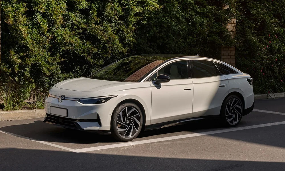 Фото Volkswagen ID 7 (2024) — вид спереди, фото 11. Белый кузов, строгая симметрия оптики — базовый ракурс знакомства с дизайном. Рисунок ходовых огней — подпись модели, по нему её узнают в потоке Volkswagen ID 7 (2024) — вид спереди, фото 11