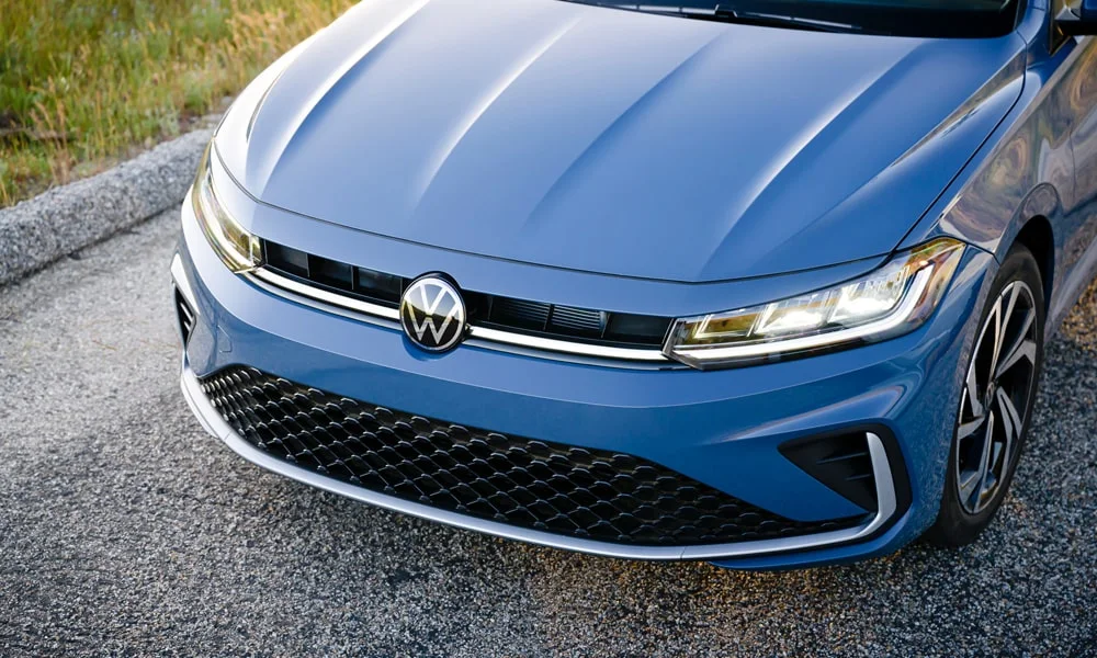 Фото Volkswagen Jetta (2024) — вид спереди, фото 11. Синий кузов, строгая симметрия оптики — базовый ракурс знакомства с дизайном. Дневные ходовые огни включаются автоматически с запуском Volkswagen Jetta (2024) — вид спереди, фото 11