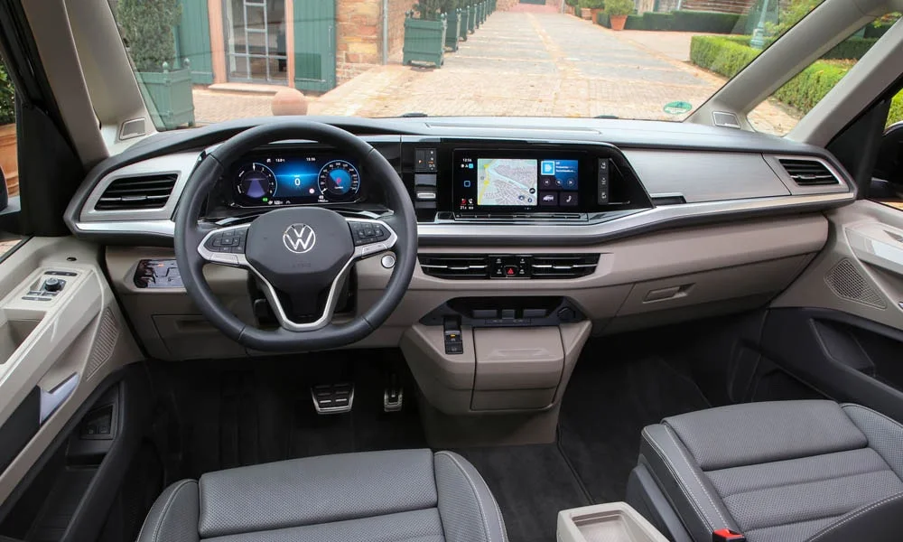 Фото Volkswagen Multivan (2024) — передняя панель. Панель в светлой бежевой отделке — видна компоновка экранов и органов управления. Мягкие материалы верхнего яруса и вставки задают уровень интерьера Volkswagen Multivan (2024) — передняя панель