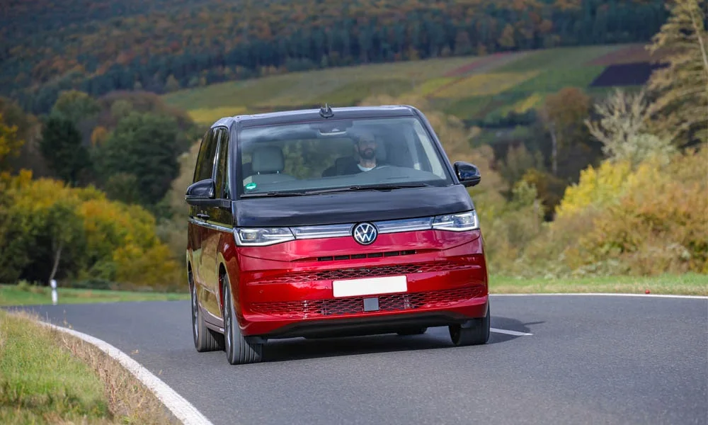 Фото Volkswagen Multivan (2024) — вид спереди, фото 9. Передок в красном исполнении — крупная светотехника и выразительный бампер. Рисунок ходовых огней — подпись модели, по нему её узнают в потоке Volkswagen Multivan (2024) — вид спереди, фото 9