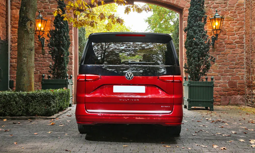Фото Volkswagen Multivan (2024) — вид сзади, фото 4. Линия крыши, стойки и задняя дверь в красном исполнении. Насадки выхлопа или их имитация внизу бампера различают версии Volkswagen Multivan (2024) — вид сзади, фото 4