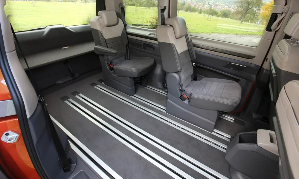 Фото Volkswagen Multivan (2024) — задние сиденья, фото 3. Посадка второго ряда: подголовники и подлокотник. Крепления ISOFIX для детских кресел — в основании спинки Volkswagen Multivan (2024) — задние сиденья, фото 3