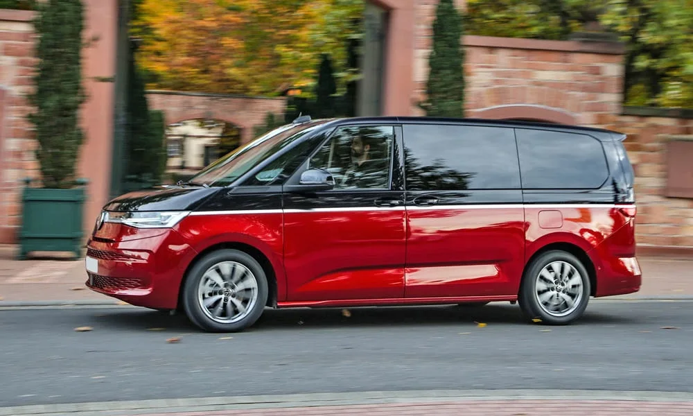 Фото Volkswagen Multivan (2024) — вид сбоку, фото 4. Сбоку читаются линия остекления и характер выштамповок на красном кузове Volkswagen Multivan (2024) — вид сбоку, фото 4