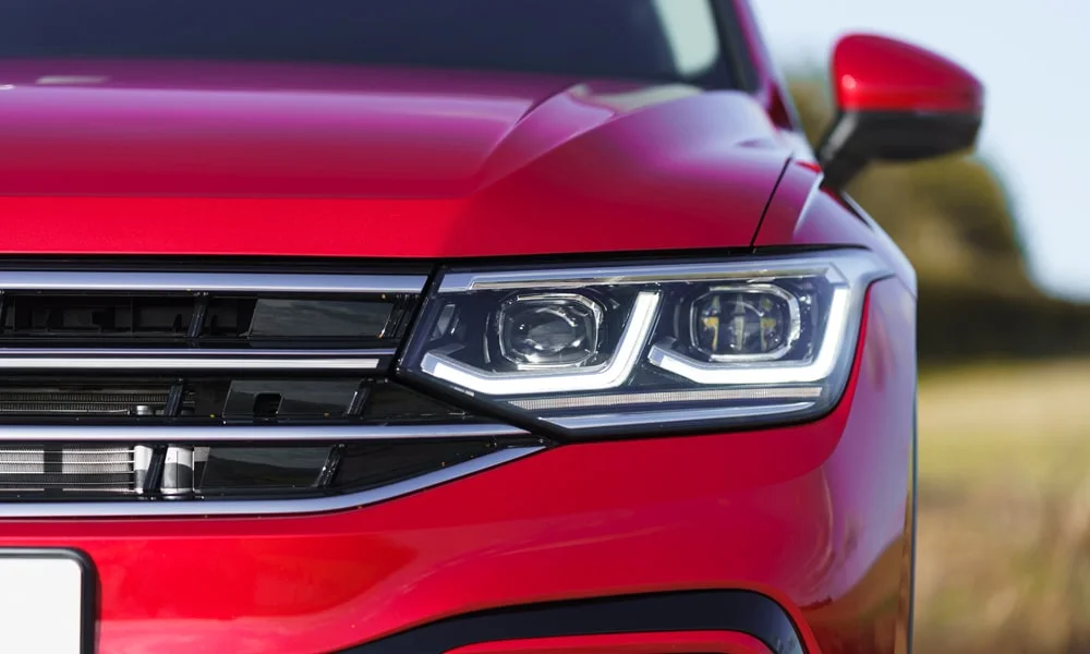 Фото Volkswagen Tiguan Allspace (2024) — вид спереди, фото 5. Красный кузов, строгая симметрия оптики — базовый ракурс знакомства с дизайном. Рисунок ходовых огней — подпись модели, по нему её узнают в потоке Volkswagen Tiguan Allspace (2024) — вид спереди, фото 5
