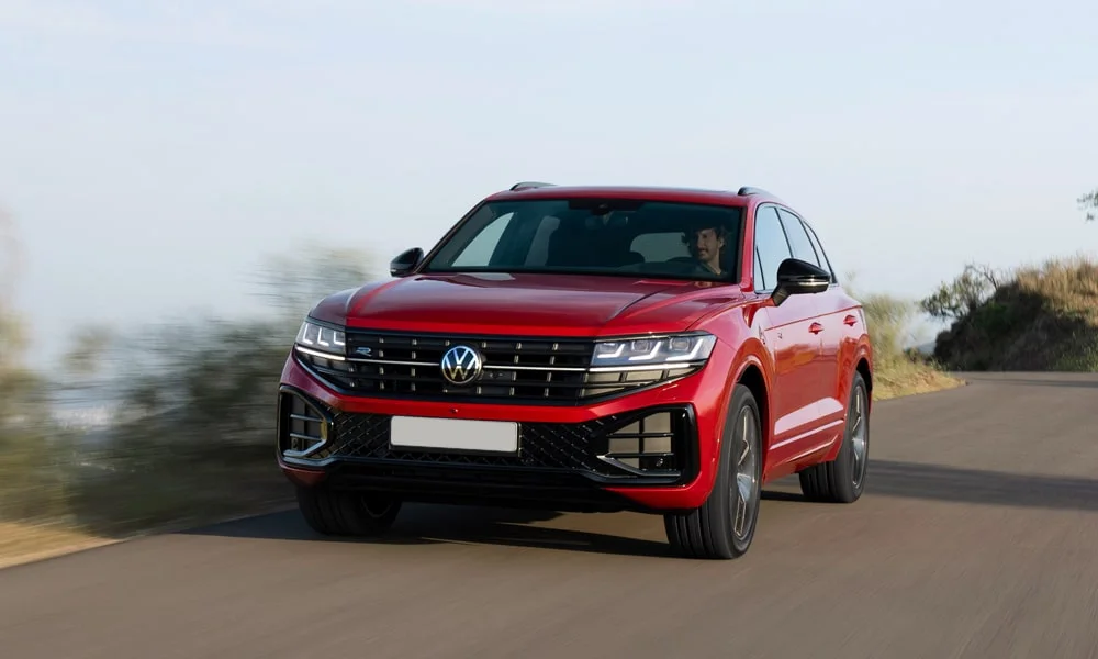 Фото Volkswagen Touareg (2024) — вид спереди, фото 9. Красный кузов, строгая симметрия оптики — базовый ракурс знакомства с дизайном. Рисунок ходовых огней — подпись модели, по нему её узнают в потоке Volkswagen Touareg (2024) — вид спереди, фото 9