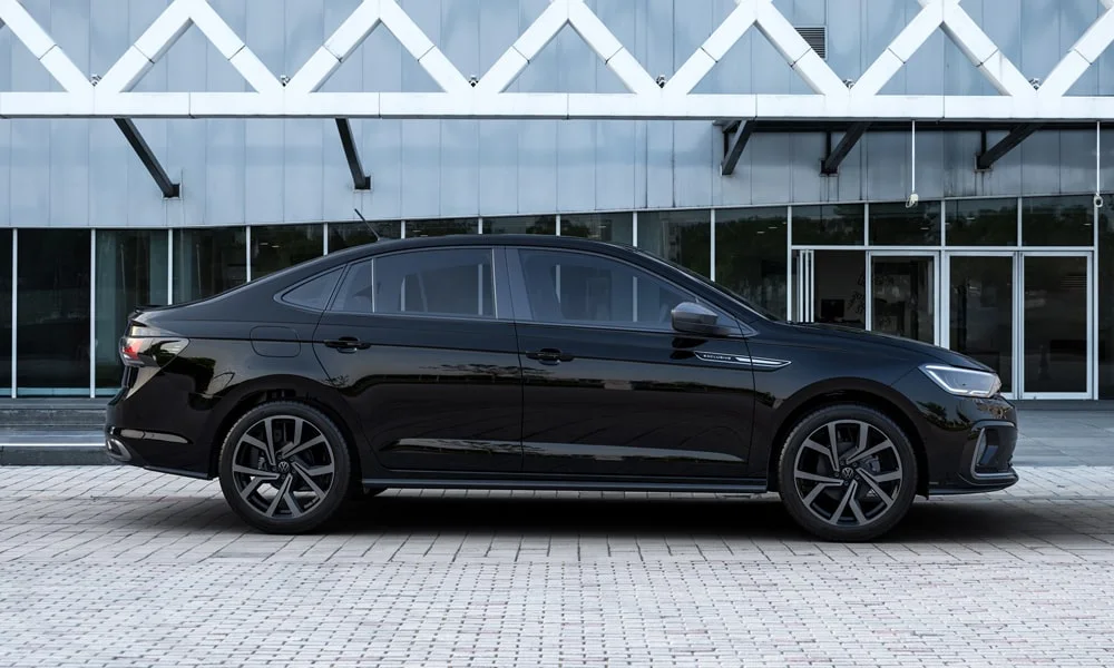 Фото Volkswagen Virtus (2024) — вид сбоку, фото 2. Сбоку читаются линия остекления и характер выштамповок на чёрном кузове. Хромированные или чёрные молдинги окон отличают комплектации Volkswagen Virtus (2024) — вид сбоку, фото 2